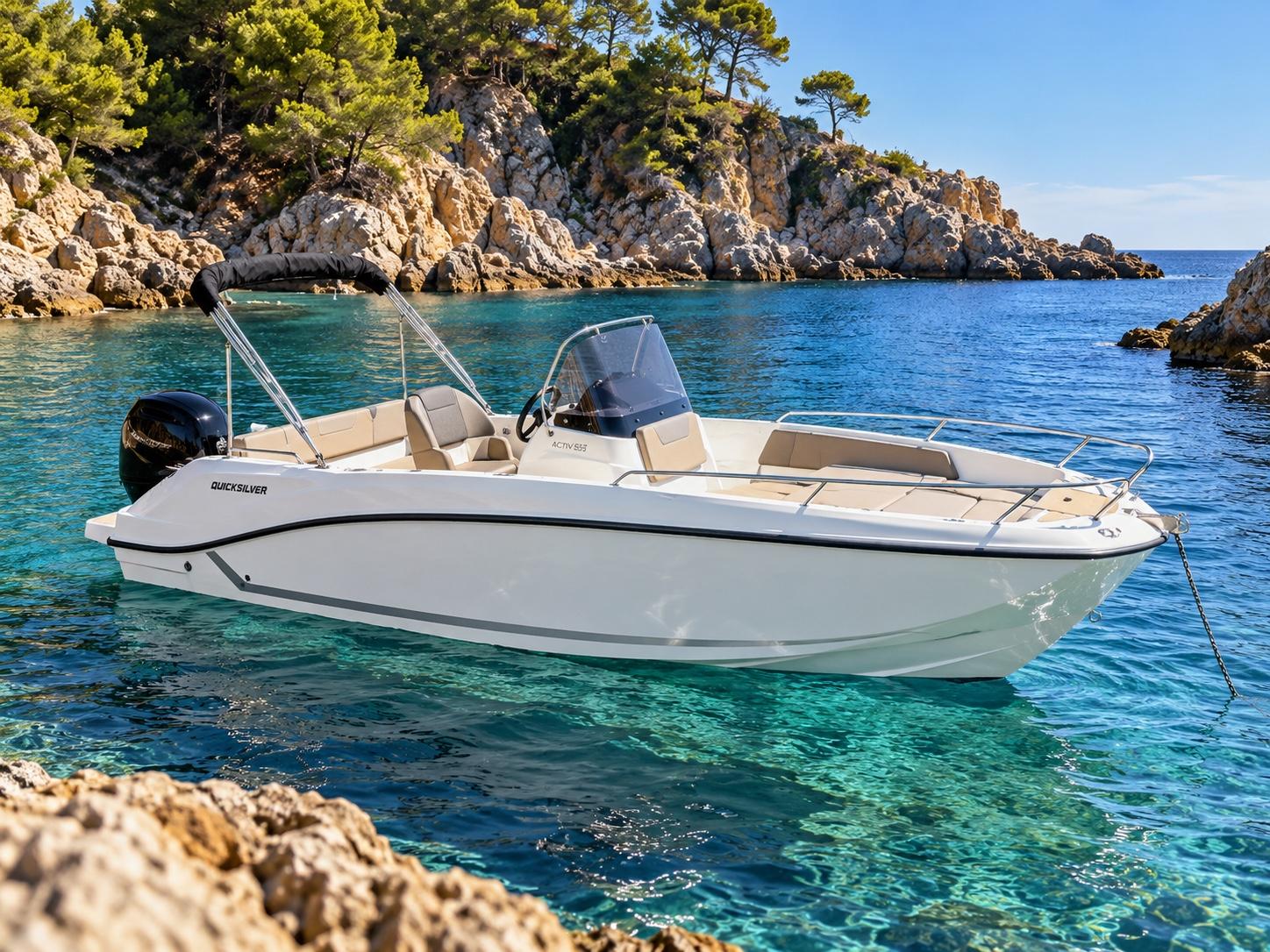 Un Quicksilver Activ 555 Open fondeado en una cala de agua transparente, entre rocas y pinos.